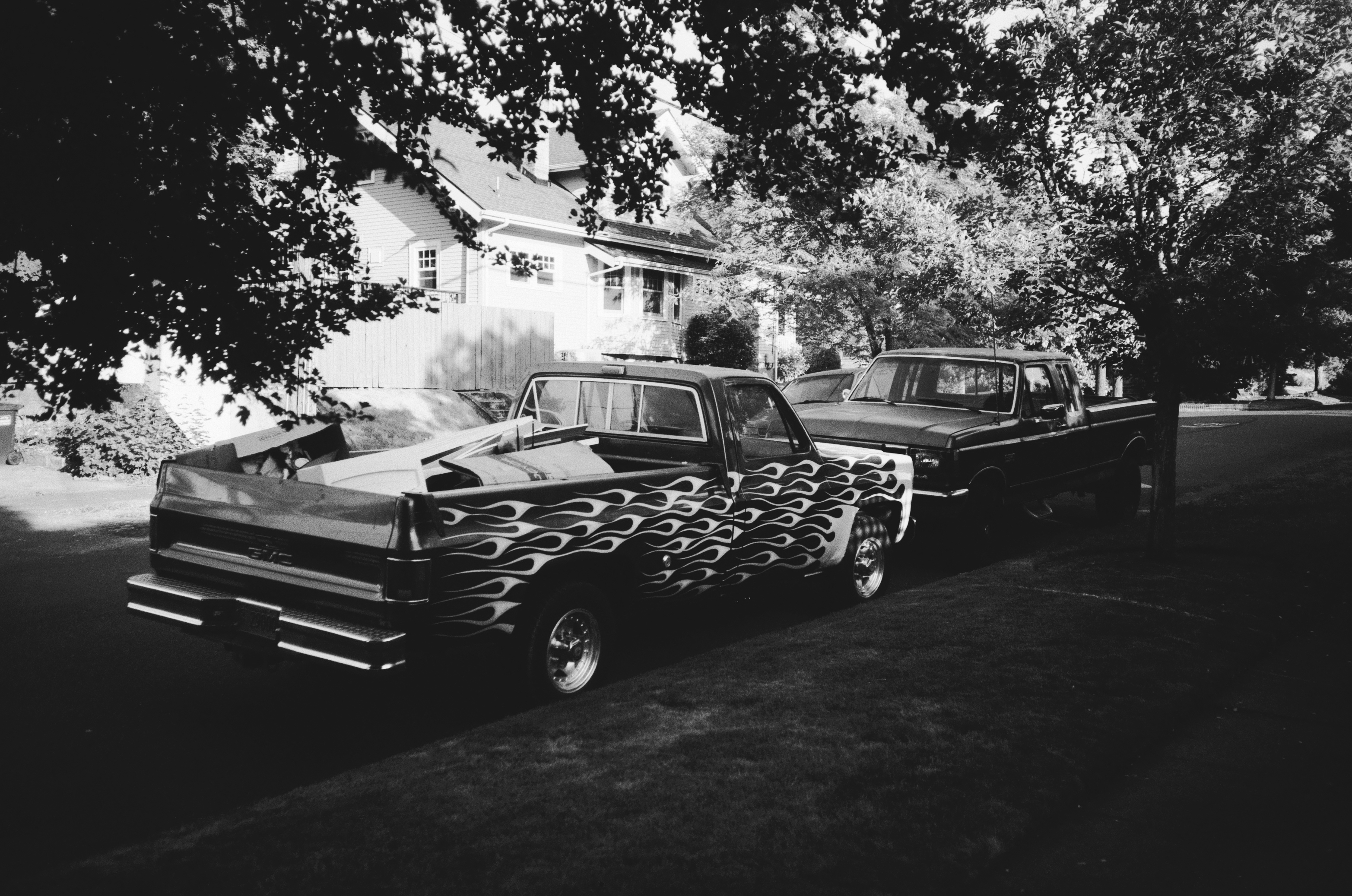 TWO PICKUP TRUCKS PARKED ALONG A RESIDENTIAL STREET, ONE ADORNED WITH FLAMES