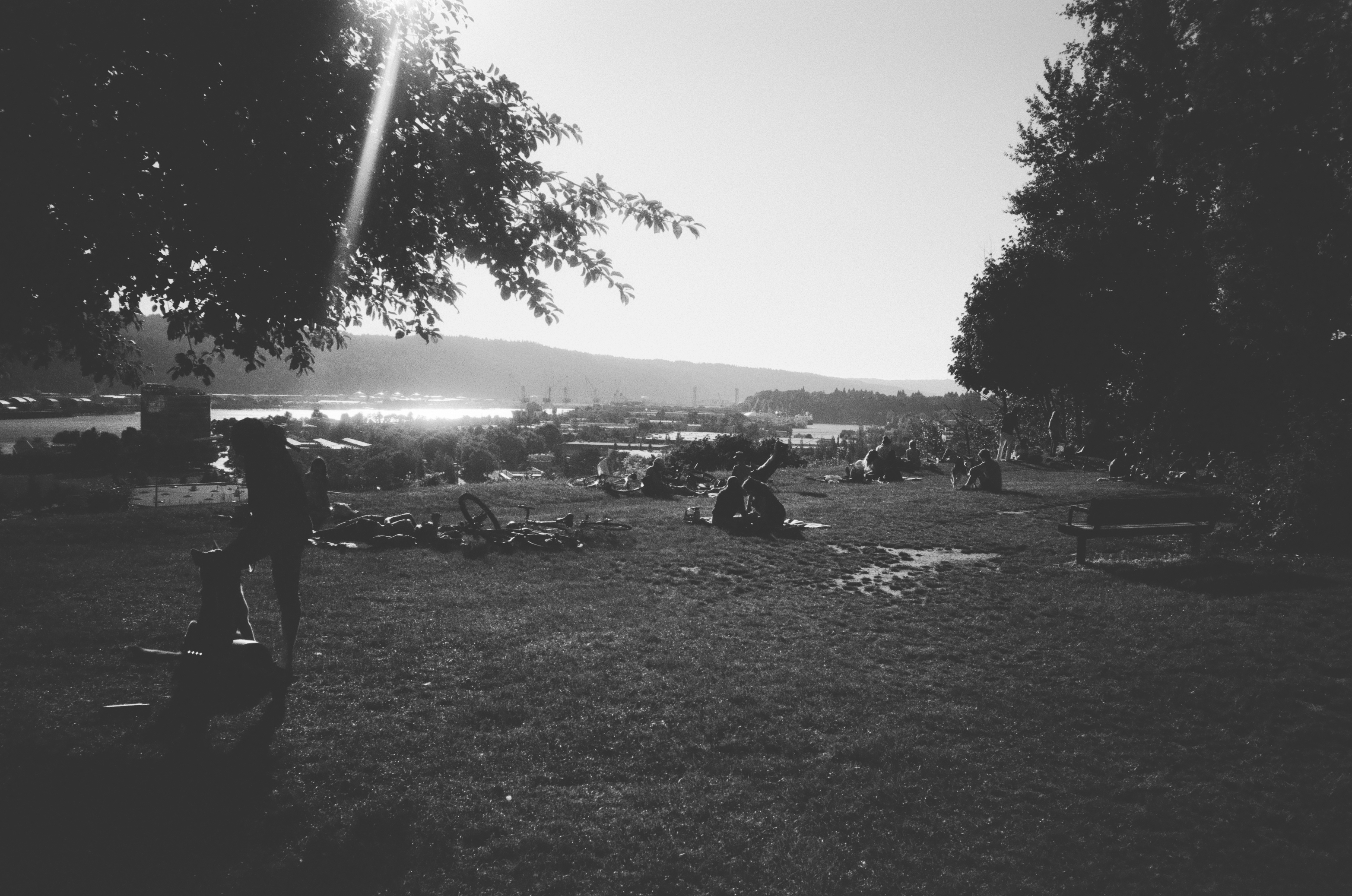 A BLACK AND WHITE IMAGE OF THE SUN SETTING AT SKIDMORE BLUFFS WITH SILHOUETTES OF PEOPLE SITTING IN THE GRASS