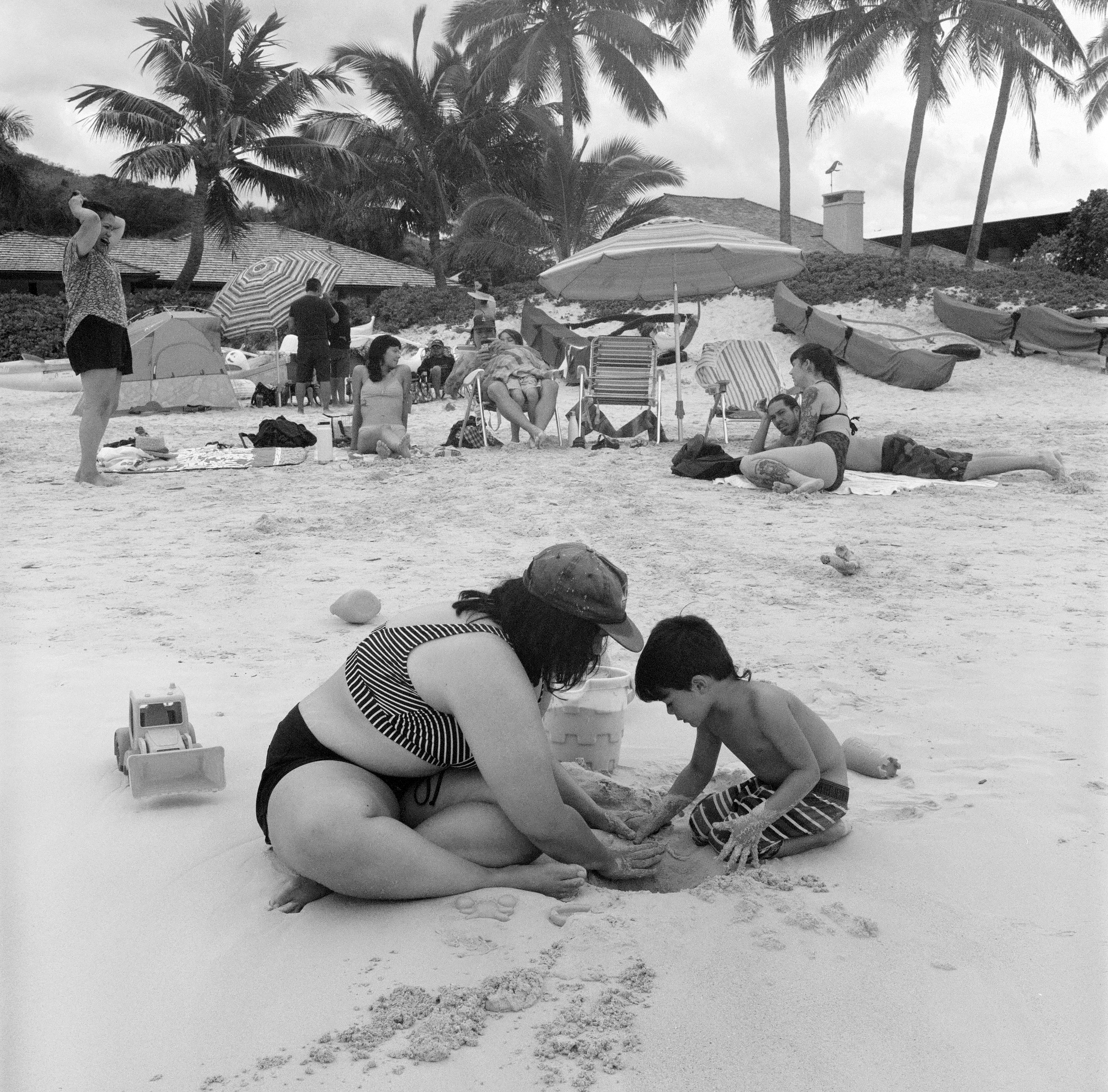 DANA AND MICAH PLAY IN THE SAND TOGETHER WHILE THE FAMILY SITS BEHIND ON CHAIRS AND TOWELS
