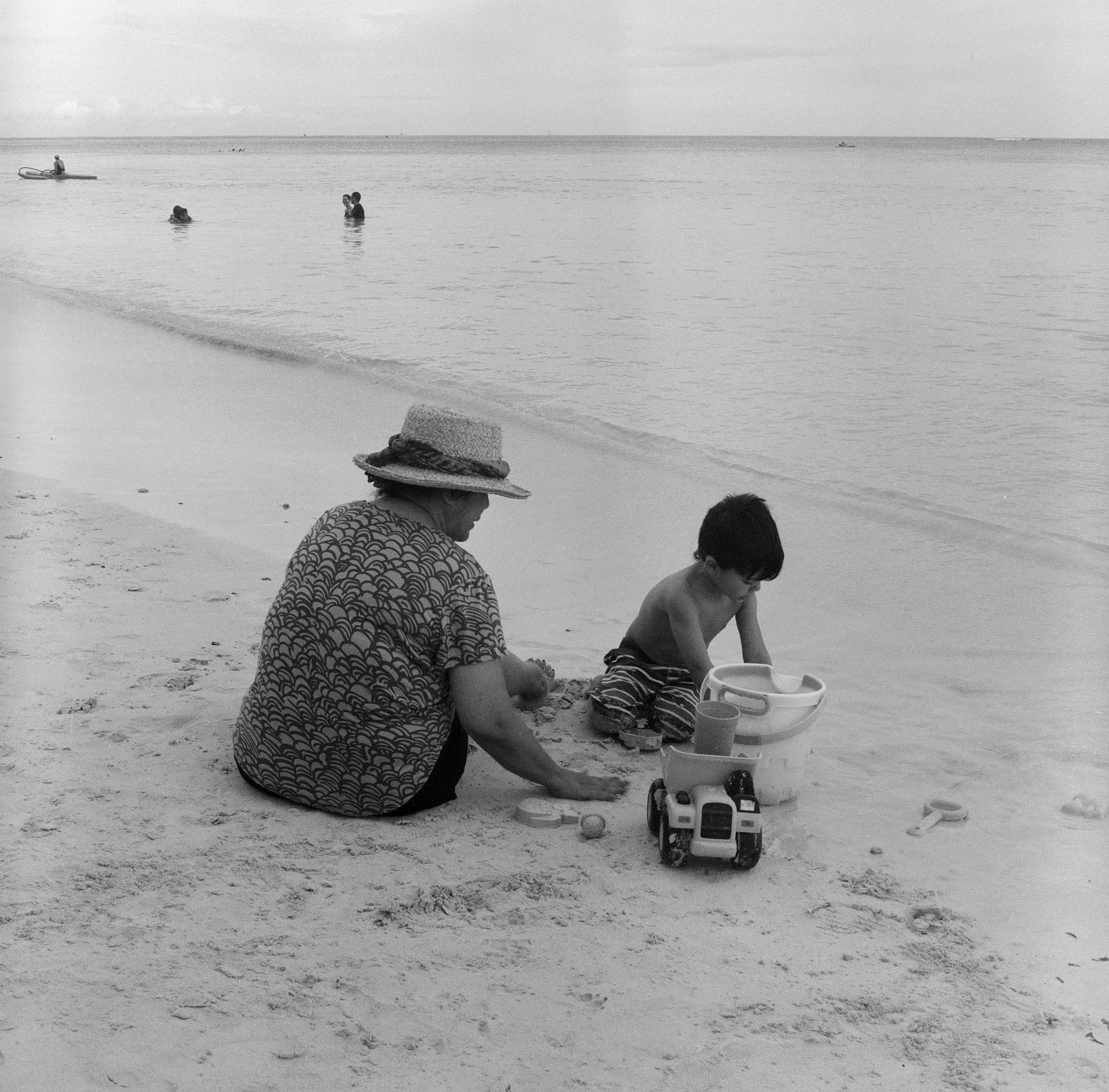 JAS AND MICAH SIT IN THE SAND AND PLAY  WITH THE OCEAN AND HORIZON BEHIND THEM