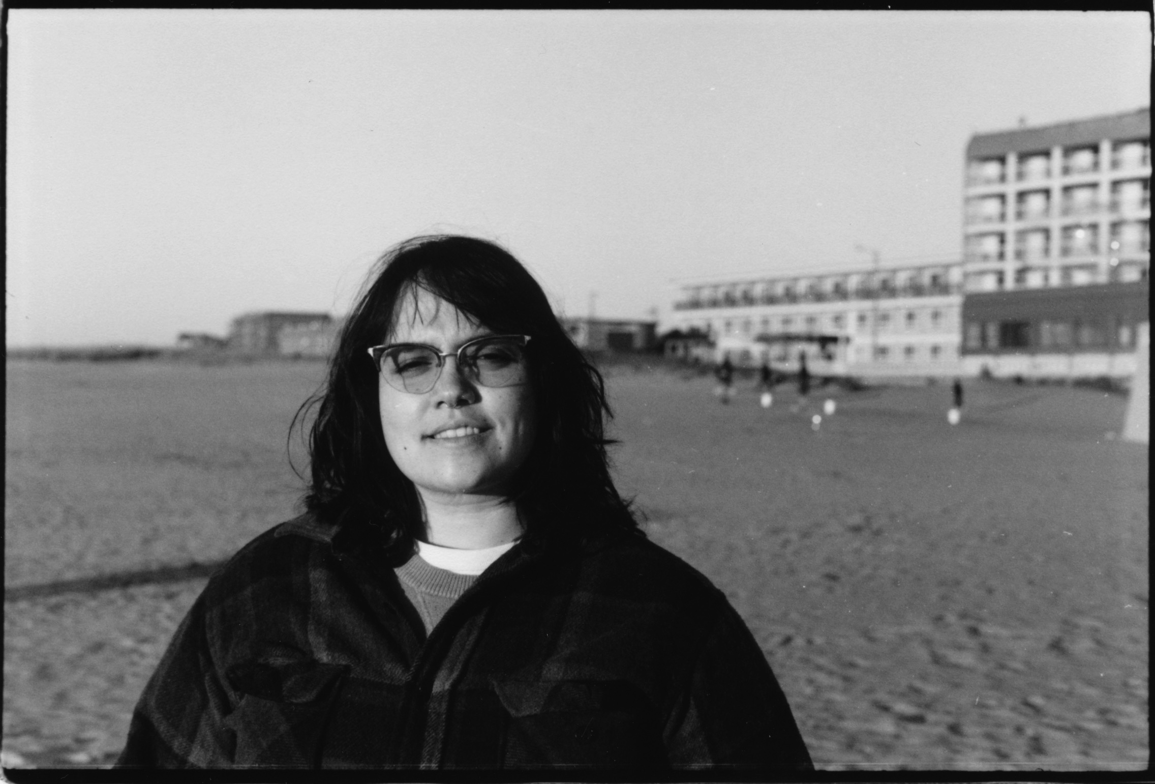 A BLACK AND WHITE PORTRAIT OF A PERSON AT THE BEACH IN FRONT OF SAND AND A HOTEL