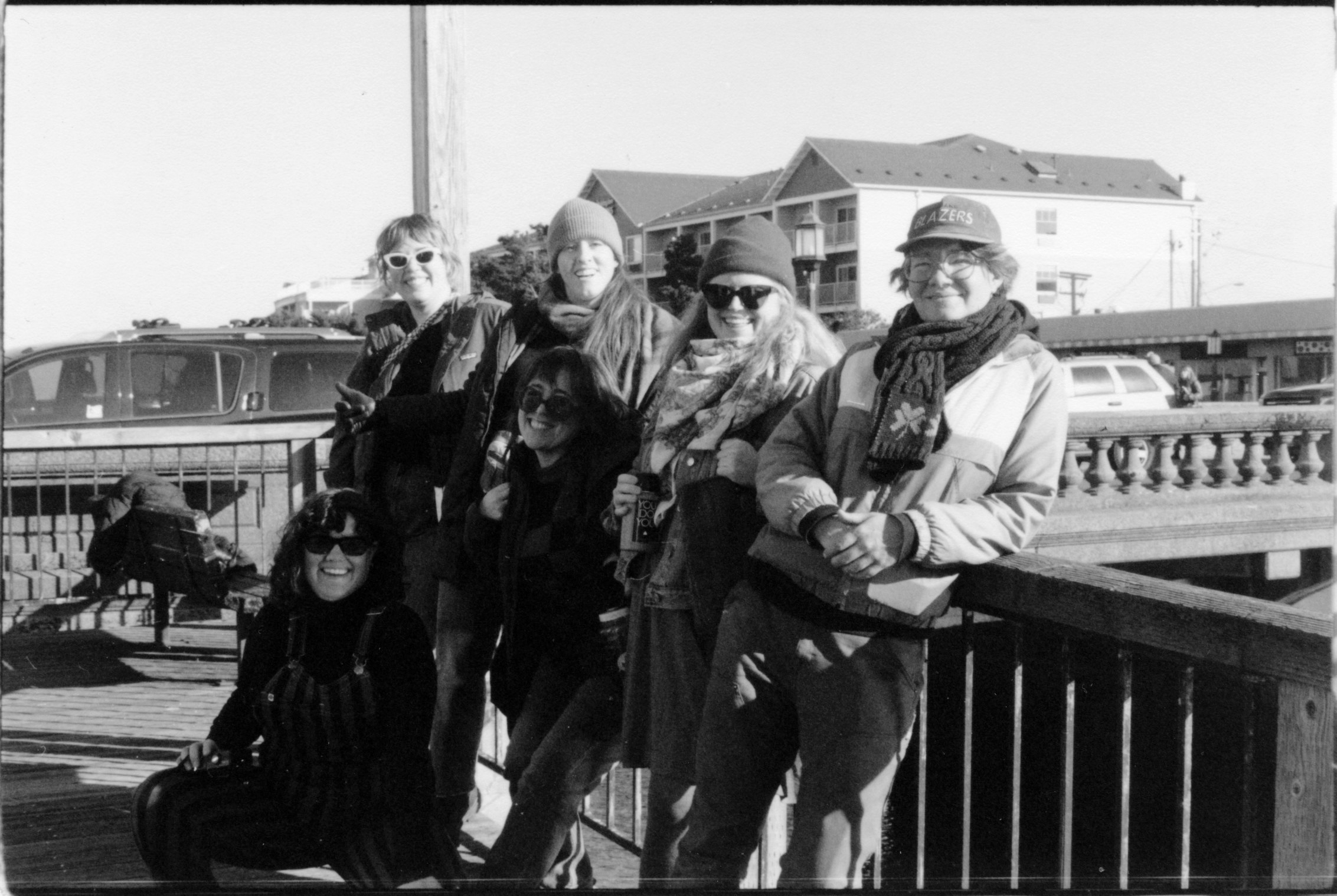 SIX WOMEN POSING AGAINST A RAIL IN BRIGHT SUNLIGHT NEXT TO A BRIDGE