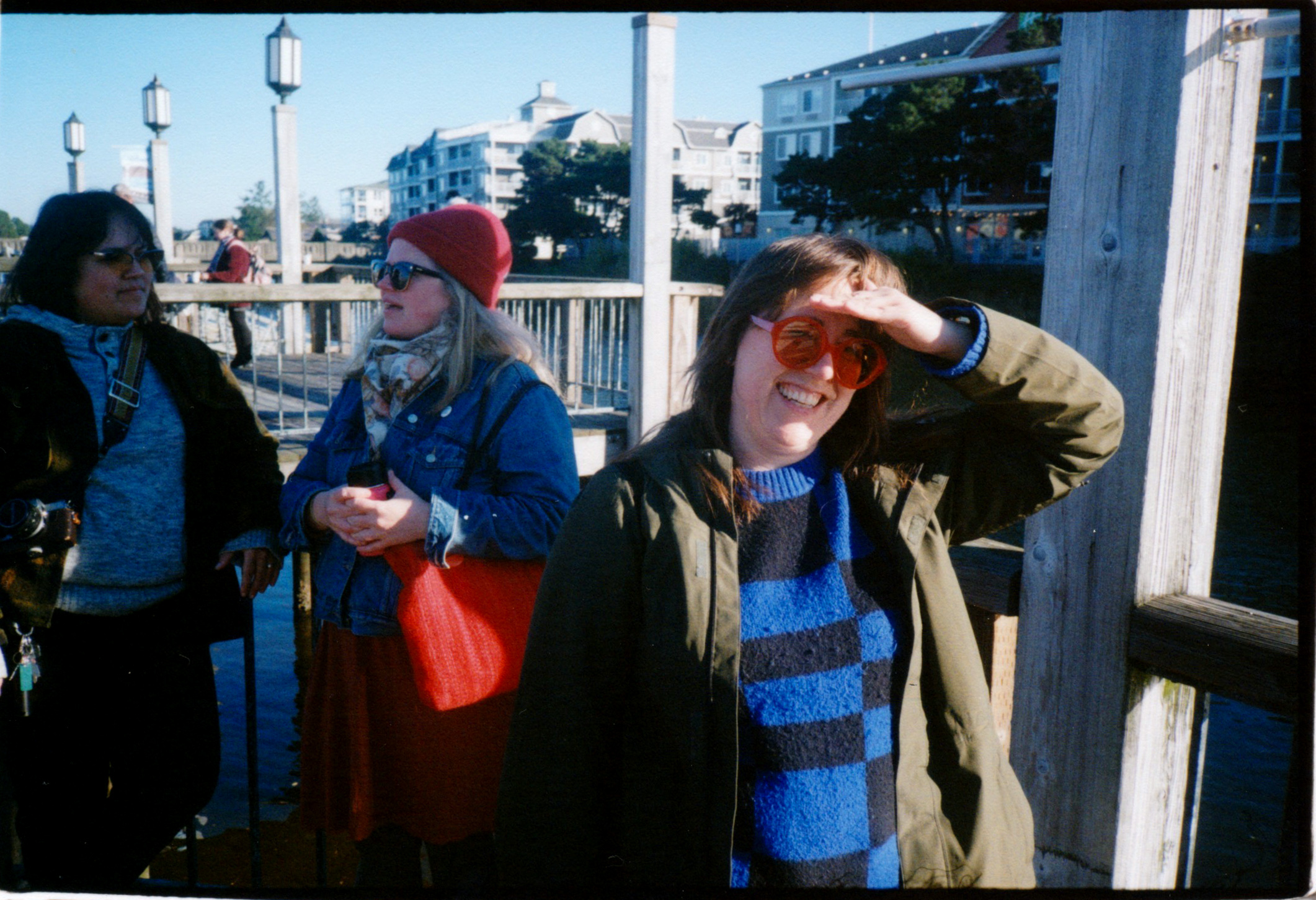A WOMAN BLOCKS HER FACE FROM THE BRIGHT SUN WITH TWO FRIENDS CHATTING IN THE BACKGROUND