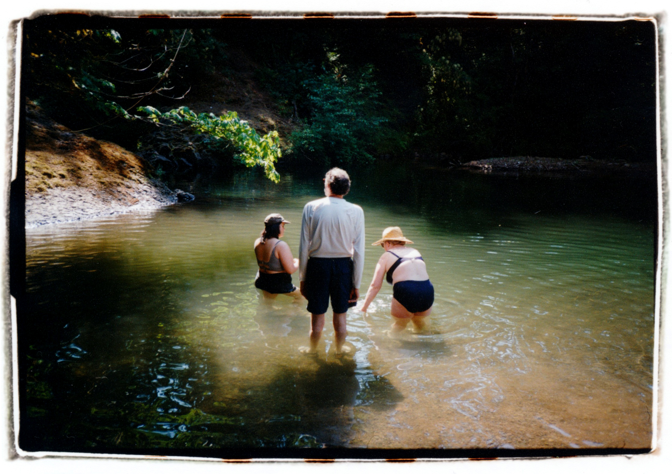 COLOR PHOTO OF 3 PEOPLE STANDING IN A RIVER SURROUNDED BY SHADE